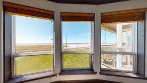 A room with three large windows overlooking a beach and a road. - OCEAN FRONT: SEASCAPE CONDO:  Seaside Vacation Homes, Inc Managed  (Seaside)