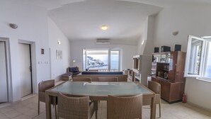 Un comedor amplio con una mesa de vidrio y sillas de mimbre, una cocina con horno empotrado, y vista al mar a través de grandes ventanales.