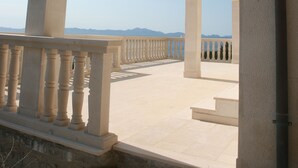 Un espacio al aire libre techado con barandilla, columnas y vistas a montañas distantes.