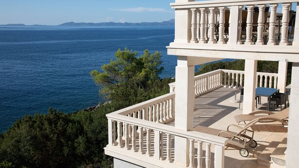 Un balcón de varios niveles con vistas al mar, mobiliario exterior y una estructura de pérgola.