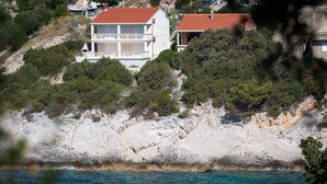 Una propiedad costera con un edificio blanco de techo rojo, ubicada en un acantilado rocoso con vista al mar.