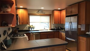 A modern kitchen with wooden cabinets, stainless steel appliances, and a large window providing natural light. - Beautiful View Home Alki Beach-West Seattle - 3 bed,3 baths (Seattle)