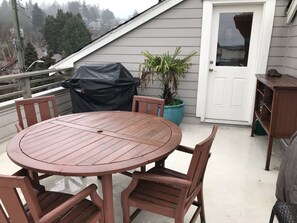 Een ronde houten tafel met vier stoelen op een balkon. Een barbecue is afgedekt met een zwarte doek.