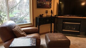 A living room with a leather sofa, a small coffee table, a fireplace, and a large flat-screen TV. - Beautiful View Home Alki Beach-West Seattle - 3 bed,3 baths (Seattle)