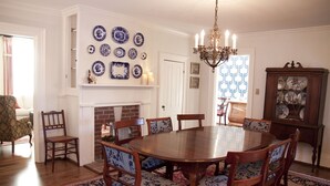A dining room with a wooden table surrounded by chairs, a fireplace, and a collection of blue and white plates on the wall.
