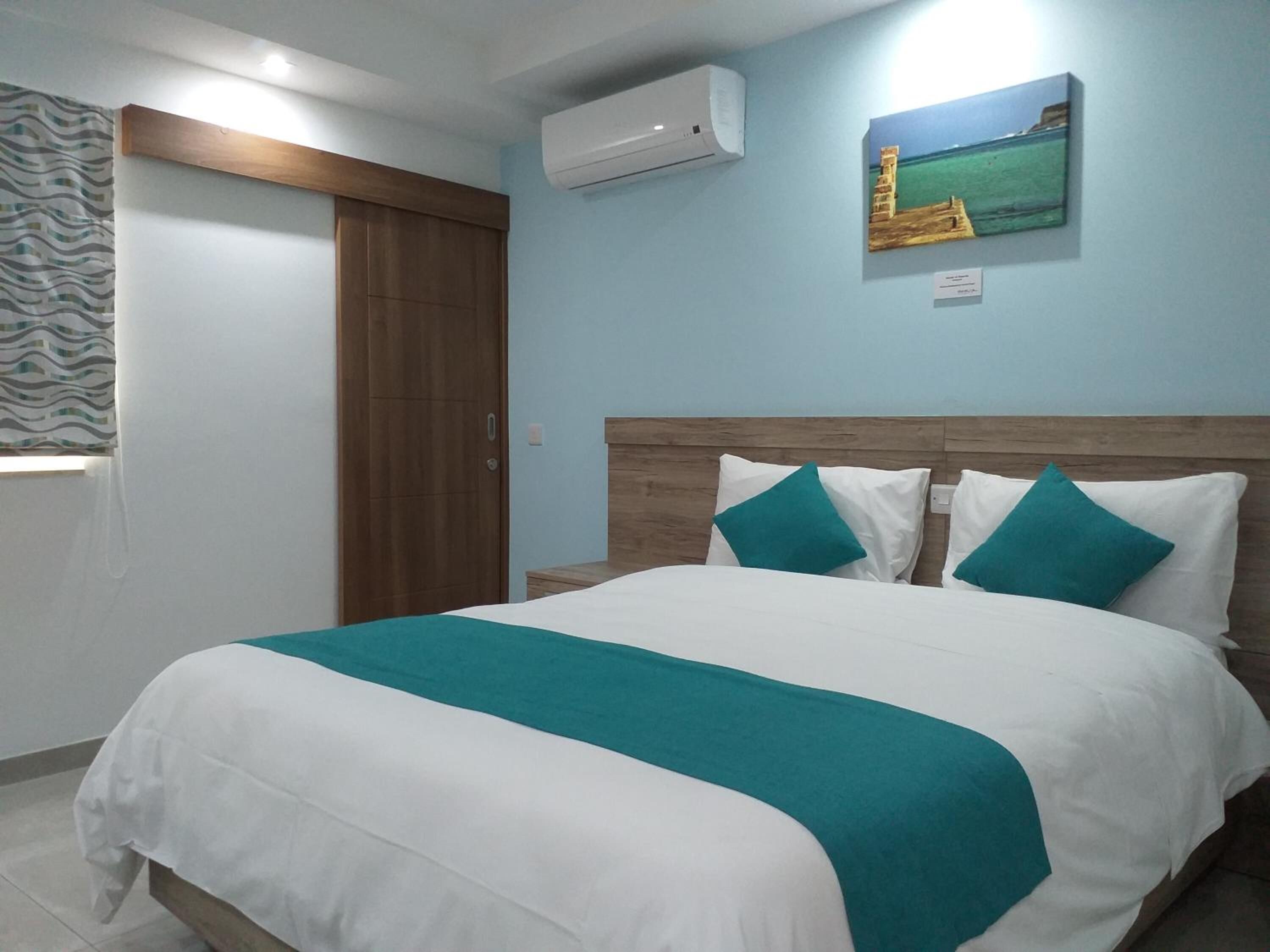 Un dormitorio con cama, cabecero de madera, aire acondicionado de pared y un cuadro de un paisaje.