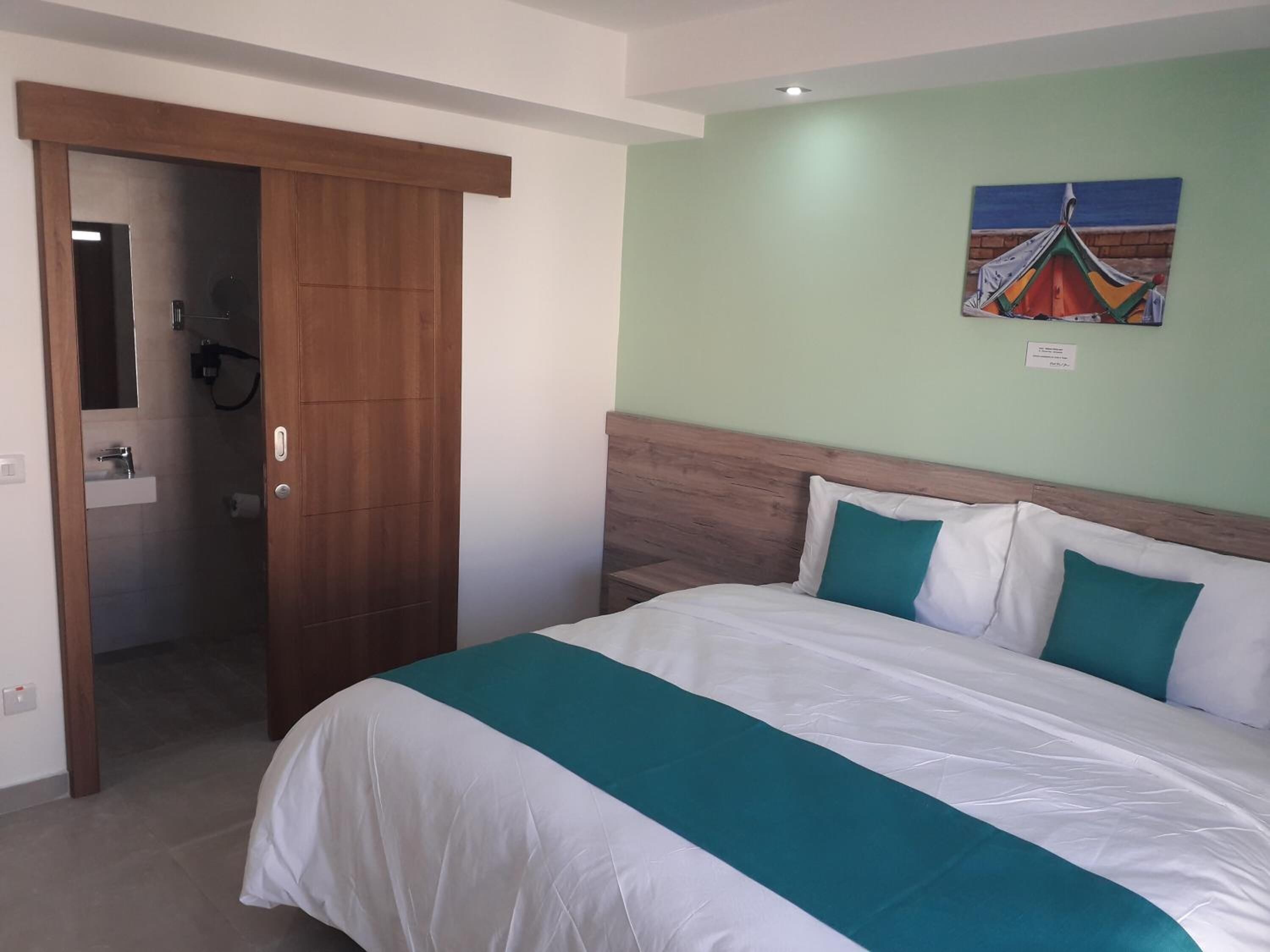 A hotel room with a bed, a wooden wardrobe, a bathroom, and a painting on the wall.