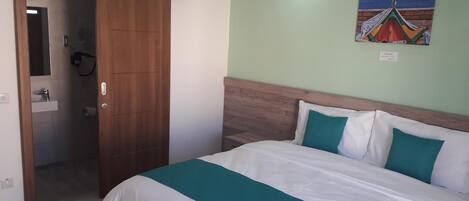 A hotel room with a bed, a wooden wardrobe, a bathroom, and a painting on the wall.