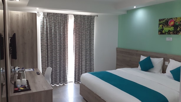 Ein Hotelzimmer mit Bett, Schreibtisch mit Stuhl, Fernseher und einem Fenster mit Vorhängen.