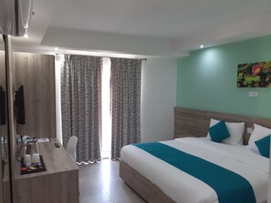 Habitación de hotel con cama, escritorio, silla, televisión y ventana con cortinas.