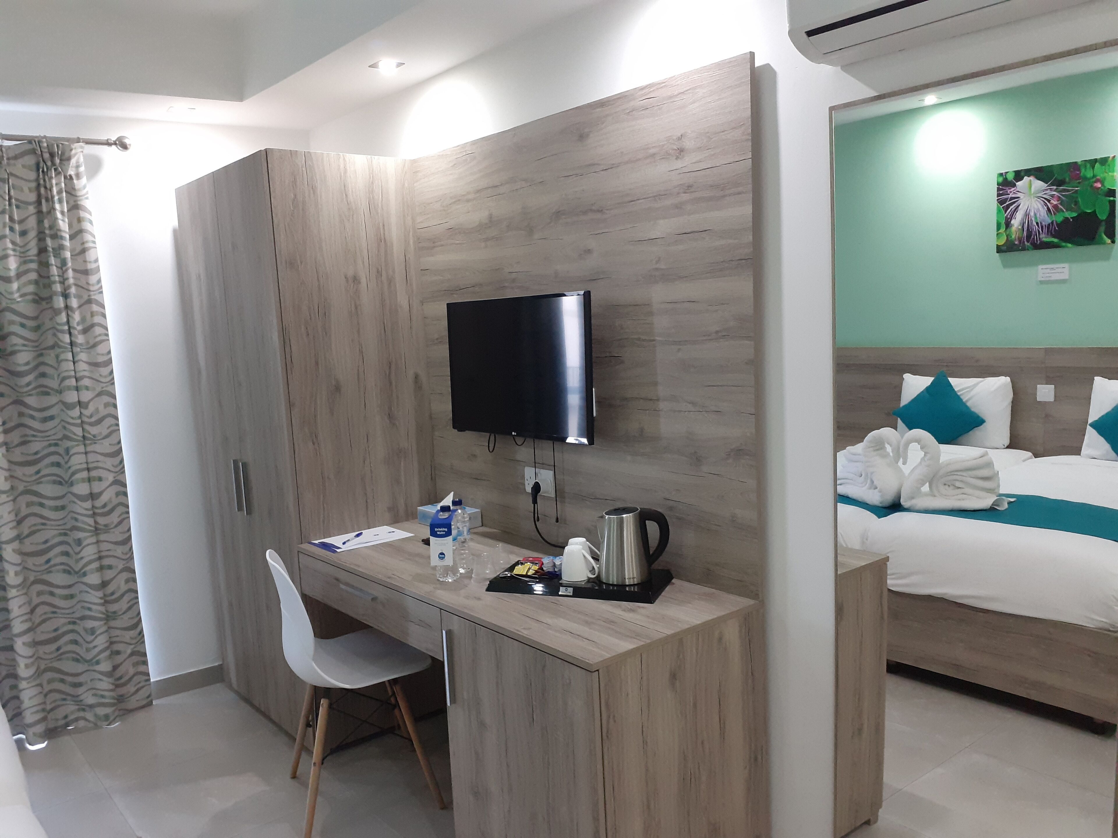 Une chambre d’hôtel avec un bureau en bois, un téléviseur à écran plat, un lit avec des oreillers bleus et un tableau au mur.