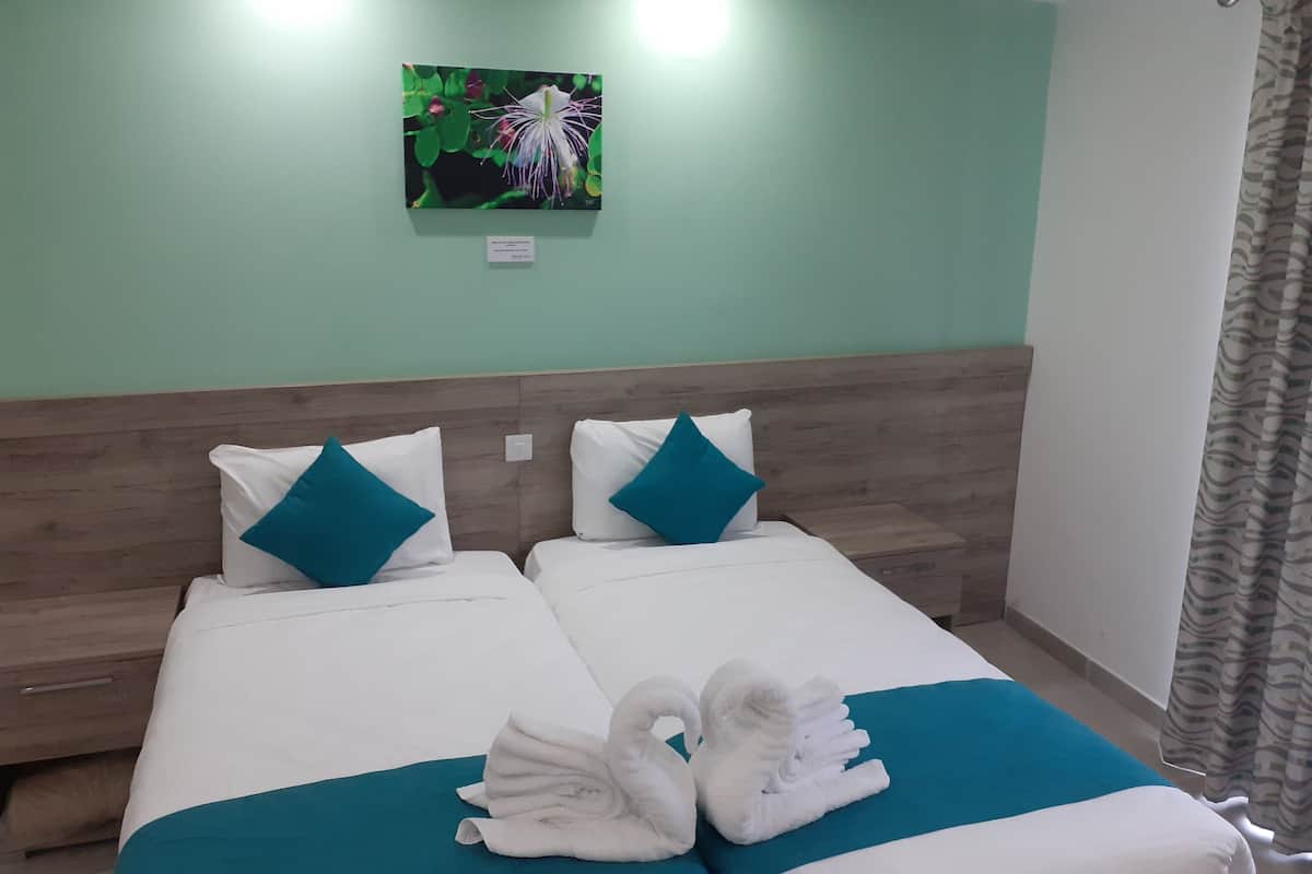 Une chambre d’hôtel avec deux lits, une literie aux couleurs turquoise et blanche, une tête de lit en bois, un tableau au mur et une décoration en forme de cygne réalisée avec des serviettes.
