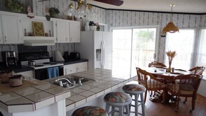Una cocina con una isla central, taburetes de bar, una mesa de comedor con sillas y un ventilador de techo.