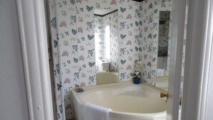 Un baño con papel tapiz floral, una bañera blanca y un espejo que refleja la habitación.