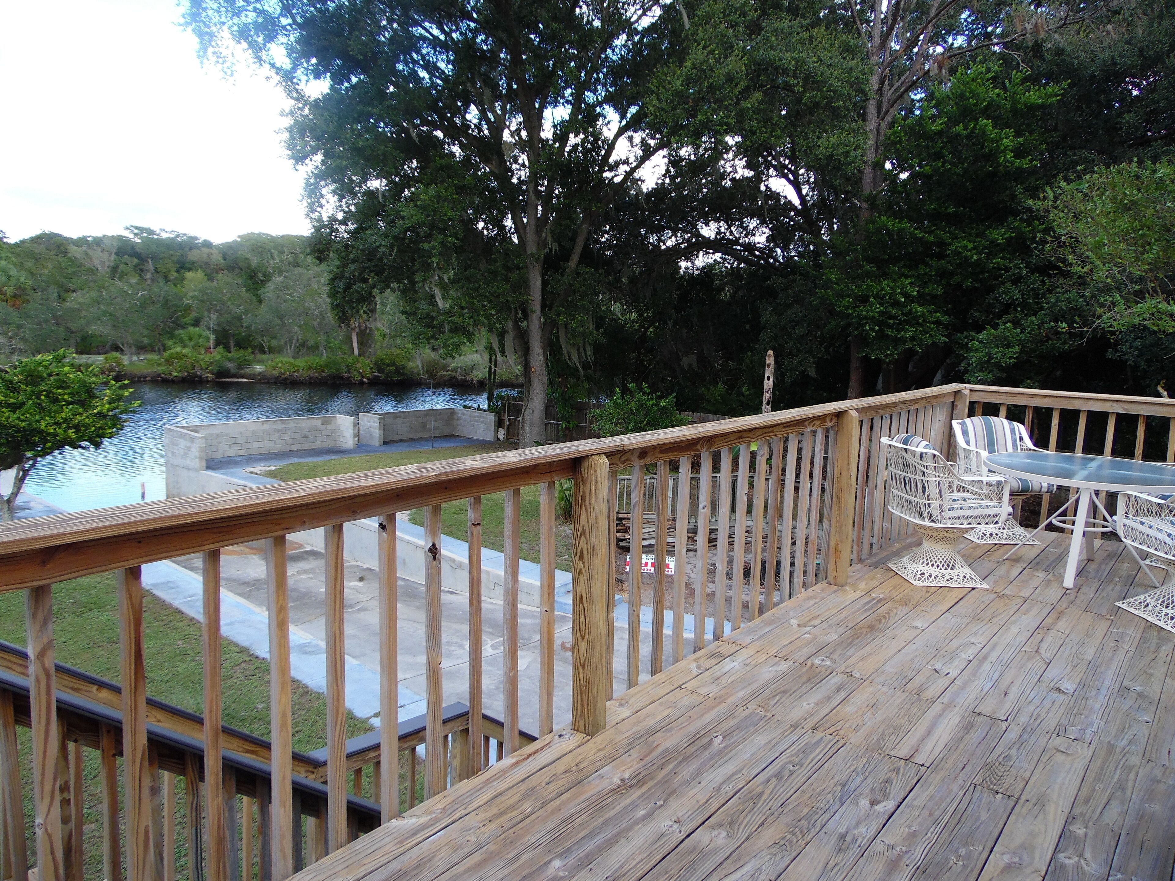 A wooden deck with outdoor furniture, overlooking a body of water and surrounded by trees.