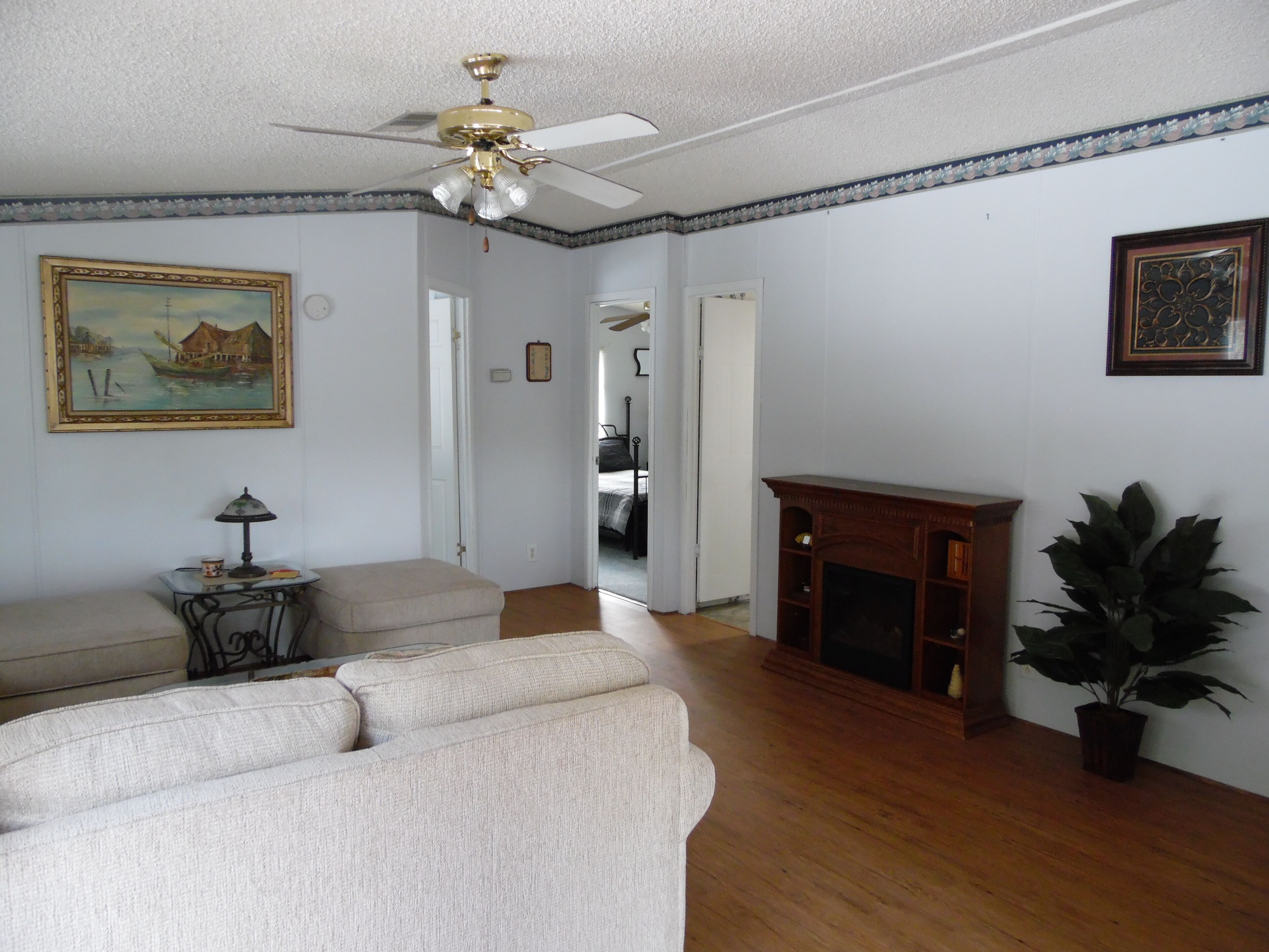 A living room with a sofa, a fireplace, a ceiling fan, and a painting on the wall.