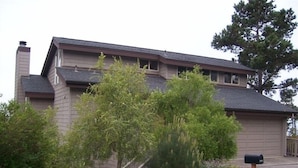 Een tweelaags huis met schoorsteen, omringd door diverse bomen en struiken.