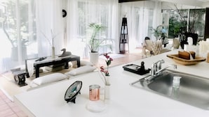 Ein modernes Wohnzimmer mit großem Fenster, einem weißen Sofa, einem Couchtisch und einer Küchenzeile mit Spüle und Holbschüssel.