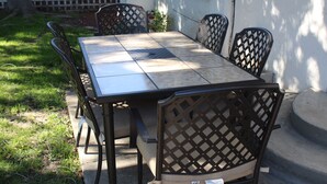 A rectangular outdoor table with a metal frame and a tiled top, surrounded by four chairs with a lattice back design. - 2BD, 1 BA, BUNGALOW FOR 9 GUESTS!! ENTIRE HOUSE W/ DRIVEWAY PARKING!! (Los Angeles)