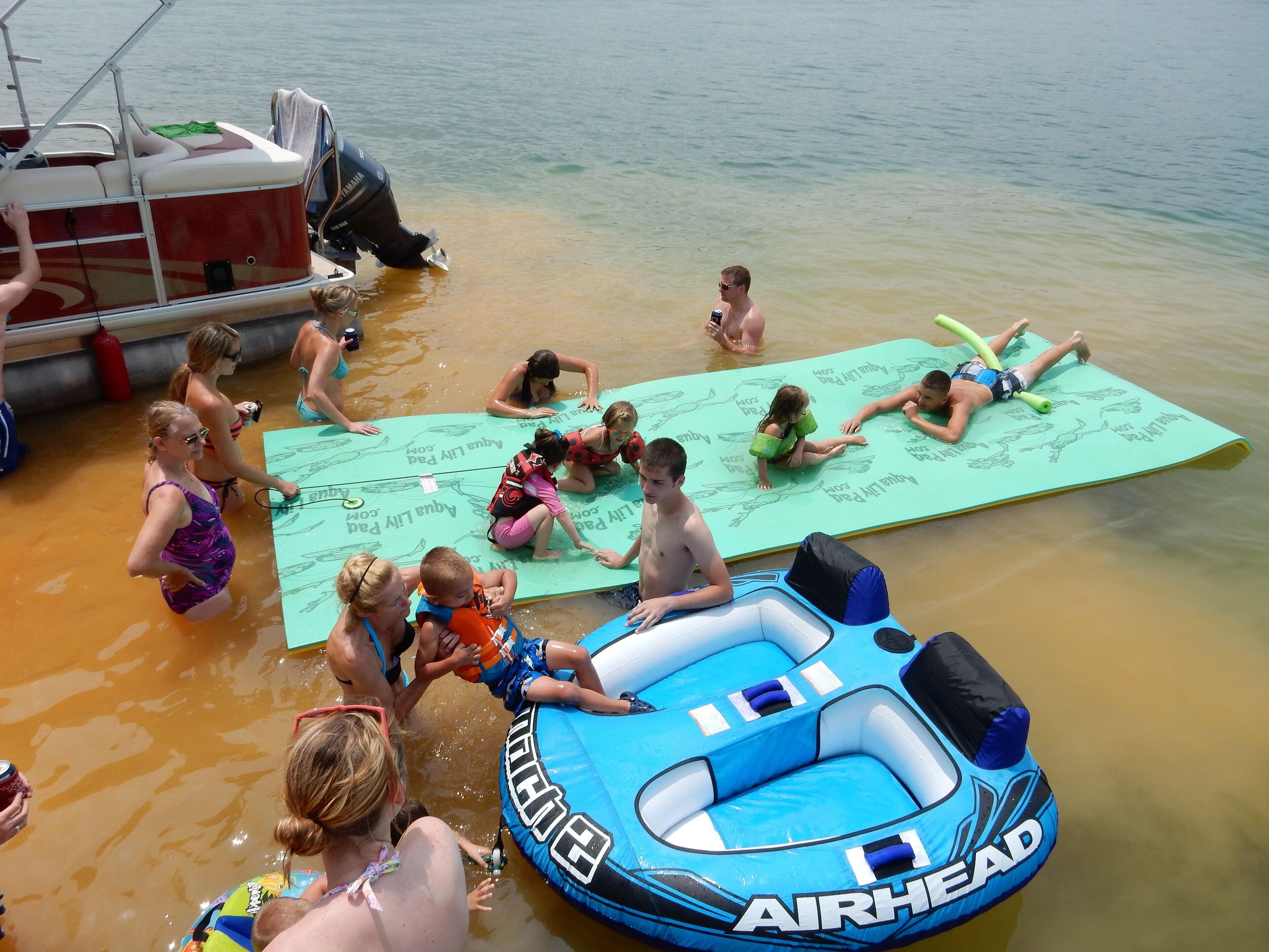 Un groupe de personnes se trouve sur un tapis flottant près d’un bateau, et un matelas gonflable est posé à proximité.