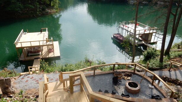 A wooden deck with a fire pit and seating area overlooking a river with boats docked. - Pirates Cove 9 Bed/9 Bath,  large hot tub,  private fire pit, double dock  (La Follette)