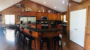 A spacious kitchen with wooden cabinets, a large island with stools, and a ceiling fan. - Pirates Cove 9 Bed/9 Bath,  large hot tub,  private fire pit, double dock  (La Follette)