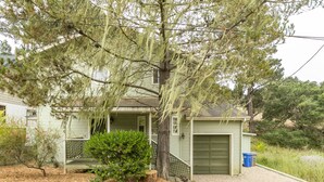 Une maison avec un garage vert, une véranda avec un banc et un petit jardin agrémenté de paillis et d’arbres.