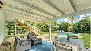 A covered outdoor area with a pool, lounge chairs, and a staircase leading to an upper level.