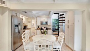 A modern kitchen with white cabinetry, a stainless steel refrigerator, and a dining area with white chairs and a table.
