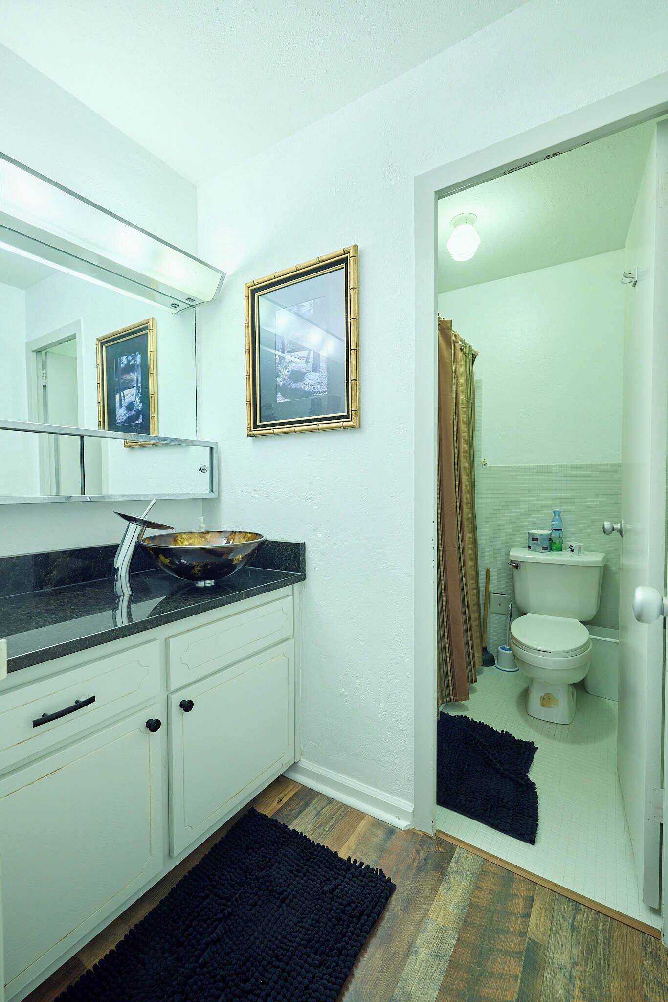 A bathroom with a white vanity, a black sink, a mirror, and a toilet.