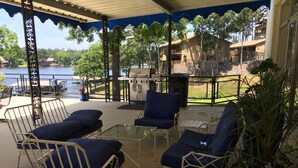 Eine überdachte Terrasse mit Gartenmöbeln, einem Grill und Blick auf einen See sowie Gebäude.