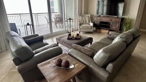 A spacious living room with a large sofa set, a coffee table, and a television. - Gulf front Beach Colony W w/seasonal beach chair/umbrella service March-October (Navarre Beach)