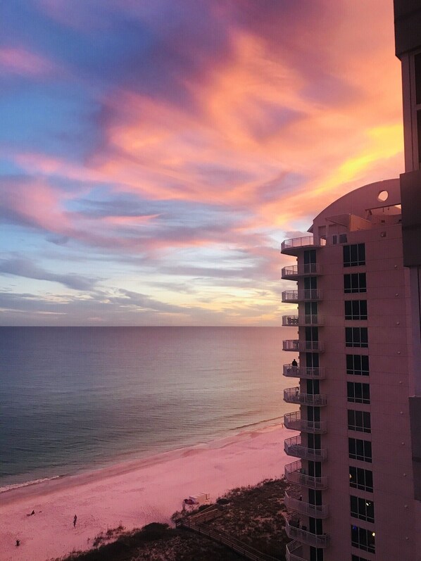 A high-rise building with multiple balconies overlooking a beach during sunset.