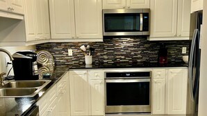 A modern kitchen with white cabinets, a stainless steel refrigerator, a microwave, an oven, and a coffee maker. - Gulf front Beach Colony W w/seasonal beach chair/umbrella service March-October (Navarre Beach)