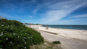 Une plage avec un ciel dégagé, un rivage sablonneux et quelques bâtiments en arrière-plan.