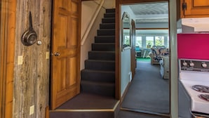 Un couloir avec une porte en bois, un escalier recouvert de moquette et un coin cuisine avec une cuisinière.