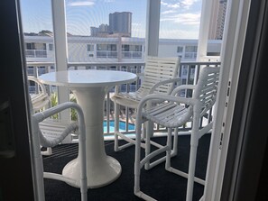 Un balcone con tavolo e sedie bianche, vista su una piscina e palazzi.