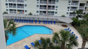 A hotel with a swimming pool surrounded by blue lounge chairs and palm trees.