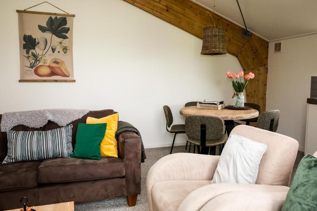 Una sala acogedora con un sofá marrón, un sofá color crema y una mesa de comedor con sillas.