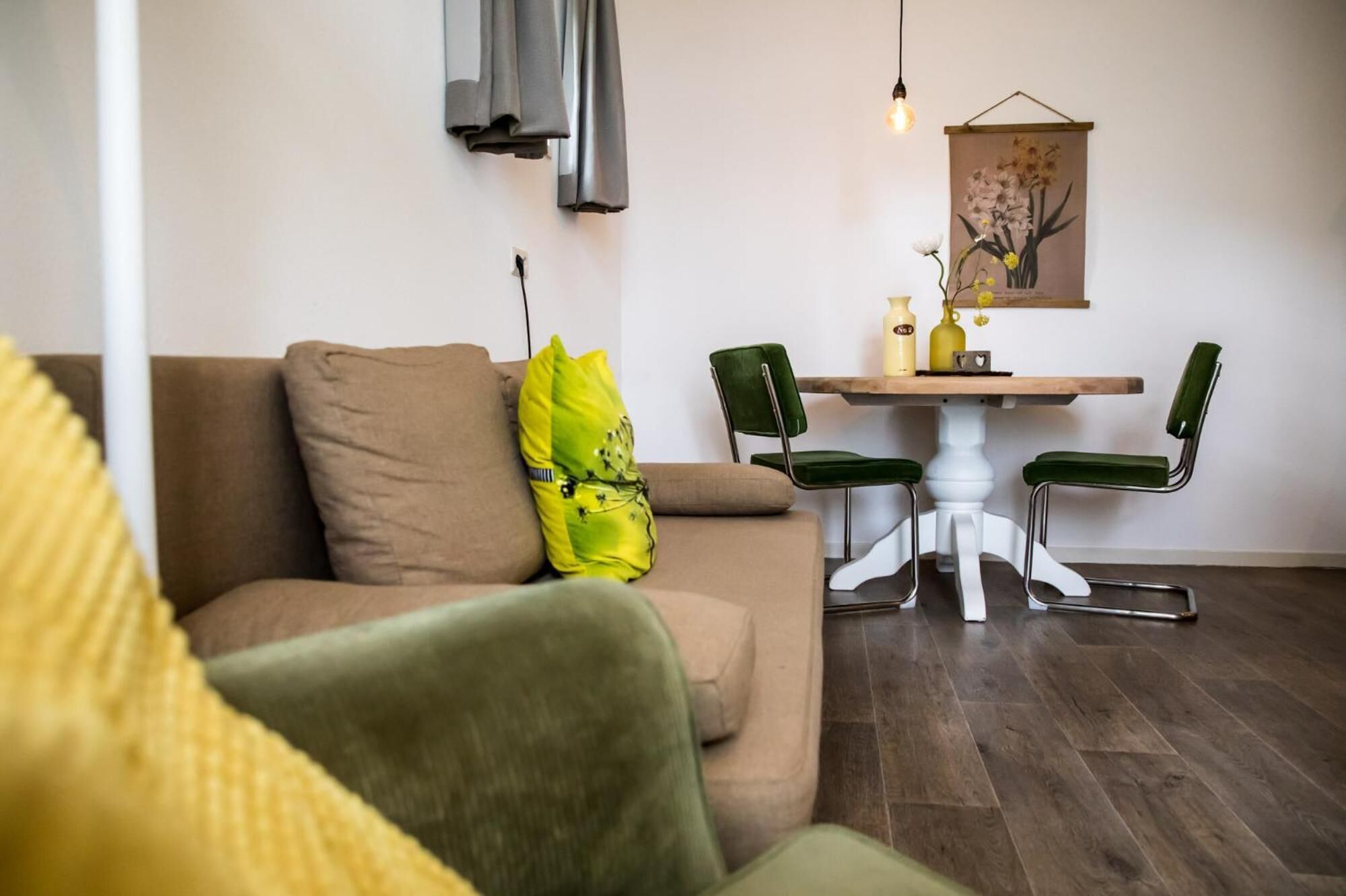 A living room with a brown sofa, green armchairs, a round wooden table, and a wall-mounted light fixture.