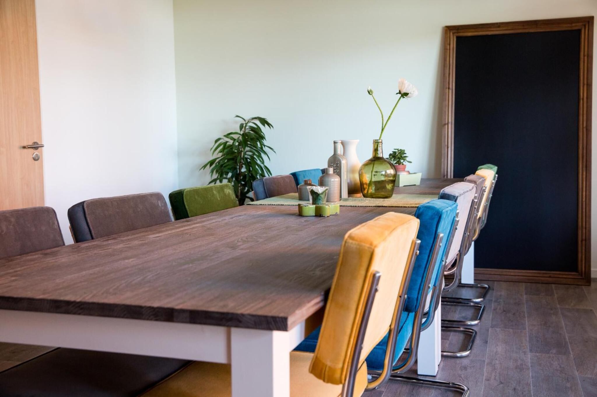 A conference room with a long table, multiple chairs, and a potted plant.