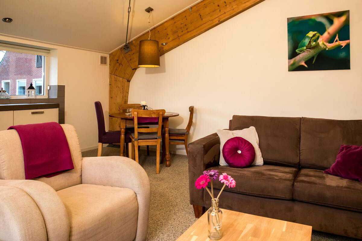Un salon chaleureux avec un canapé marron, un fauteuil beige et une table à manger en bois.