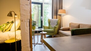 Een knus ingerichte kamer met een bed, een groene fauteuil, een klein tafeltje en een lamp.