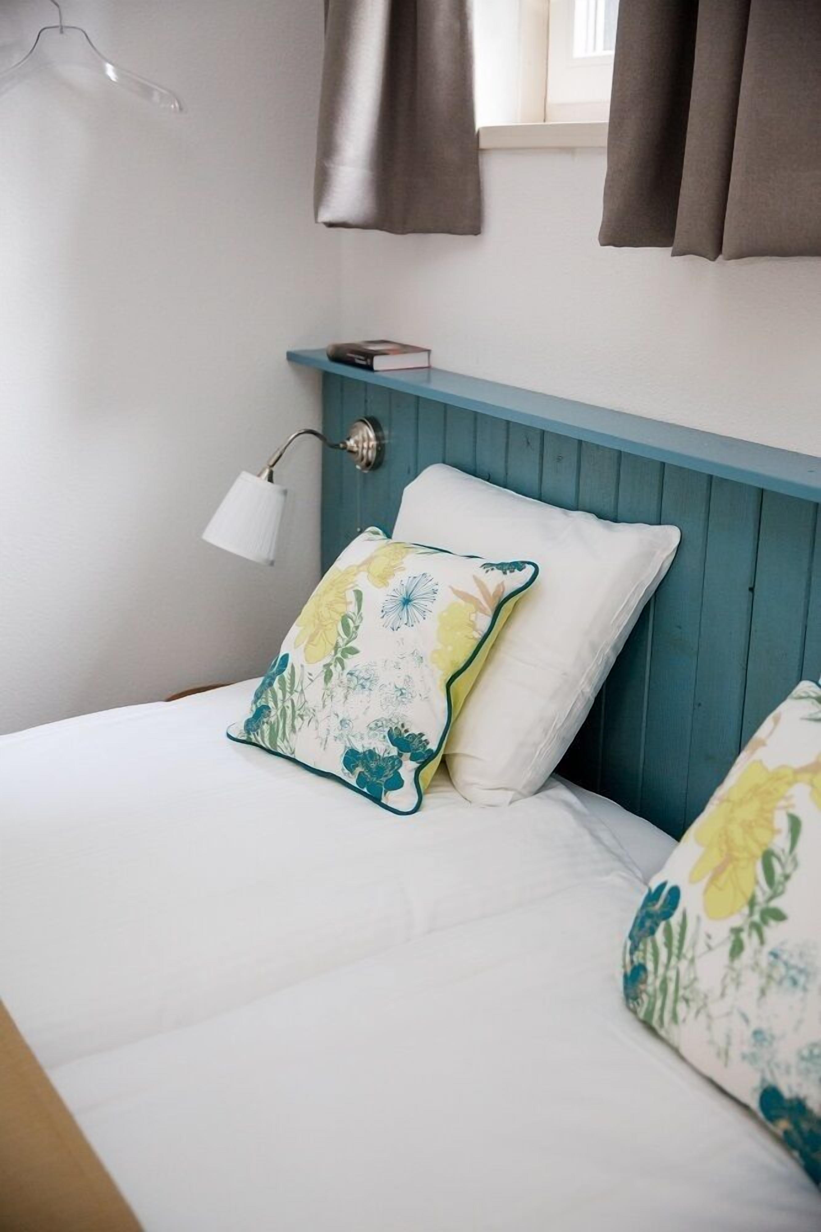 A bed with white bedding and floral pillows, a bedside lamp, and a blue headboard.