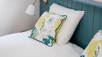 A bed with white bedding and floral pillows, a bedside lamp, and a blue headboard.
