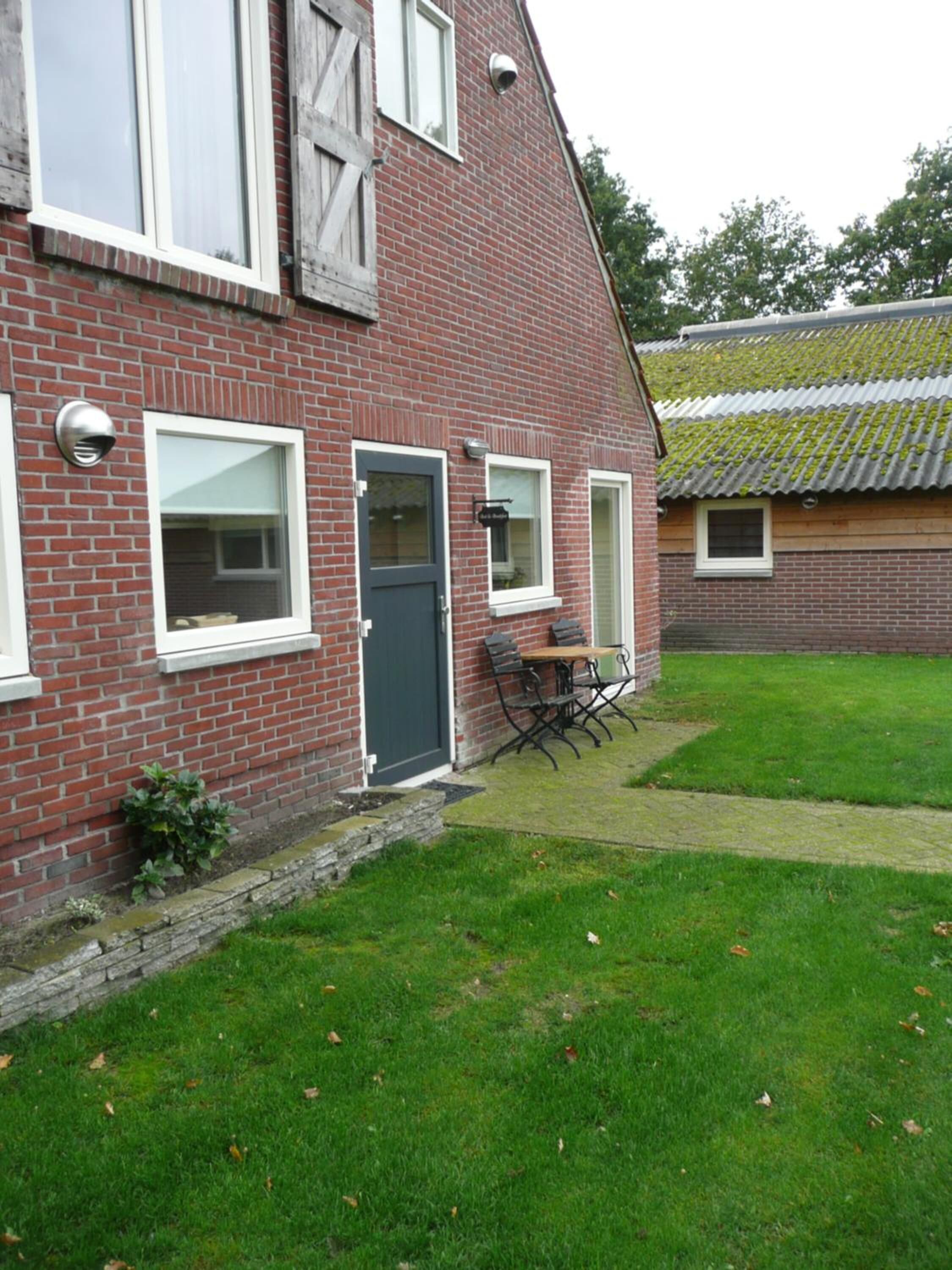 A brick house with a dark door, white-framed windows, and a small patio with a table and chairs.