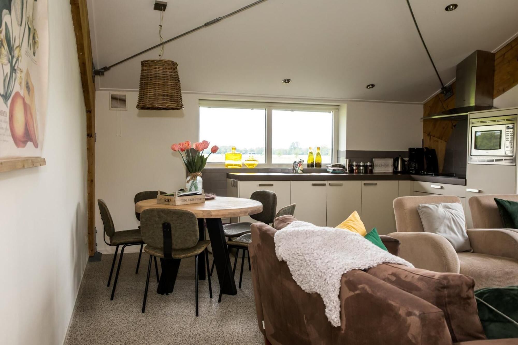 Una sala de estar acogedora con un sofá marrón, una mesa de comedor con sillas, una cocina con microondas y una ventana con vistas.