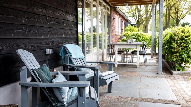 Een overdekt terras met twee Adirondack-stoelen, een tafel en stoelen.