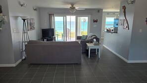 A living room with a sofa, a TV, a coffee table, and a view of the ocean.