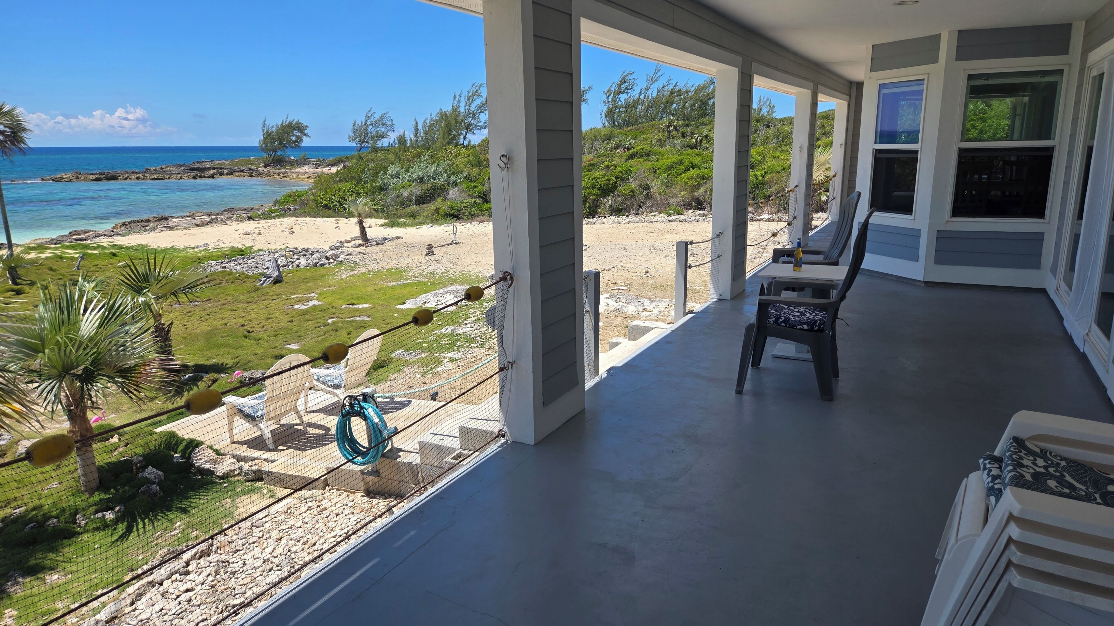 A covered porch with a view of the ocean, a chair, and a hose.